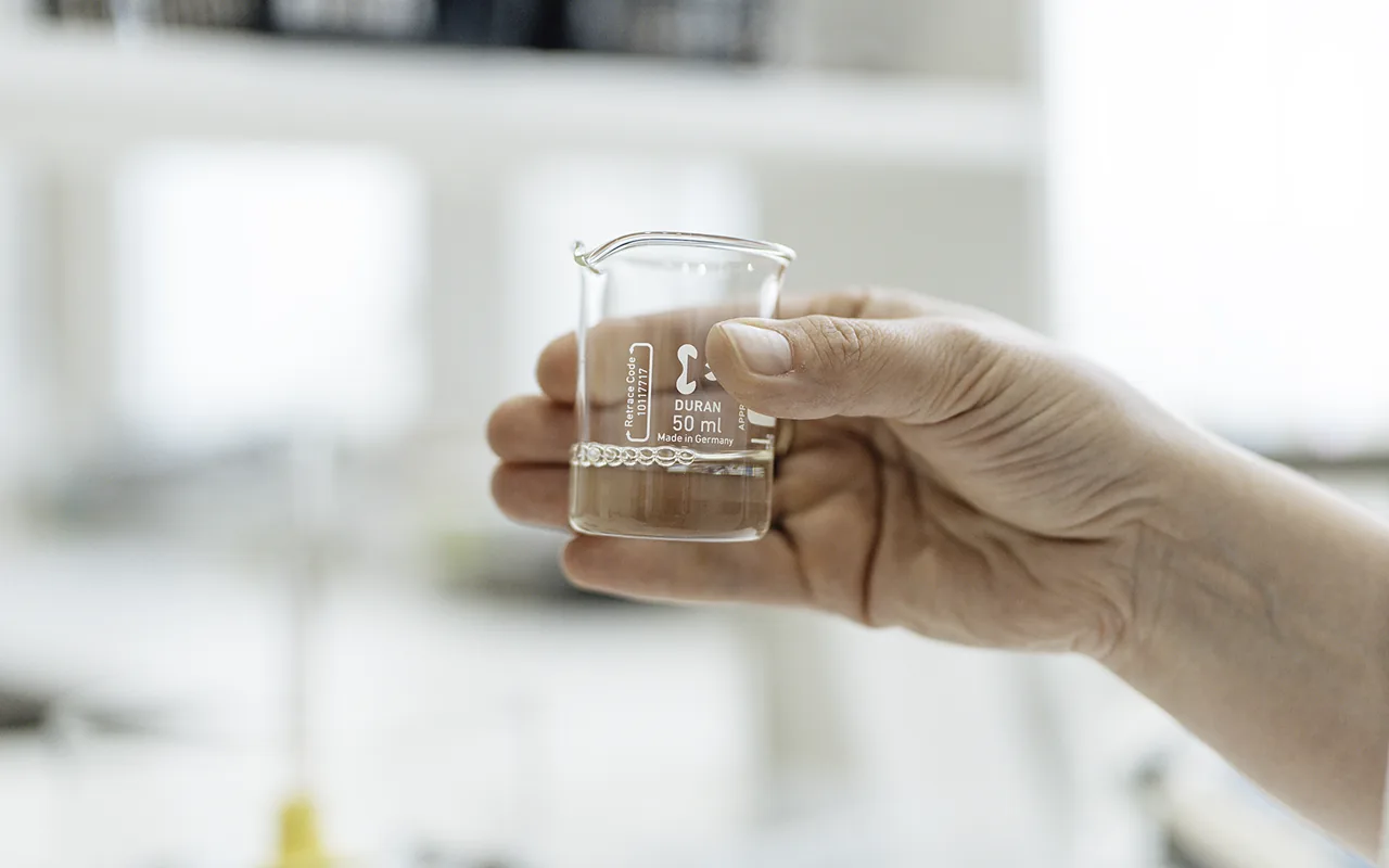 Käsi pitelee dekantterilasissa olevaa näytettä Nordic BioCosmeticin laboratoriossa Tuusulassa